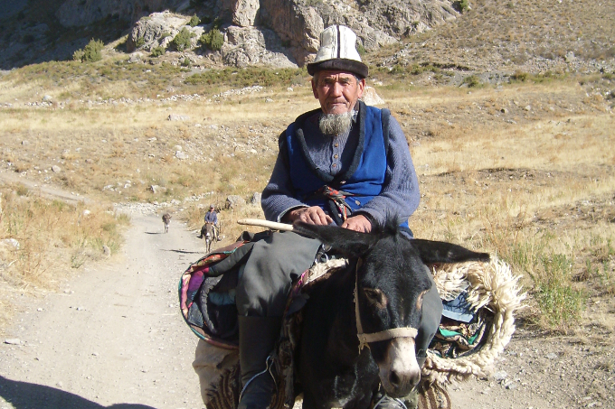 Ein Kirgise in traditioneller Kleidung reitet auf einem Esel